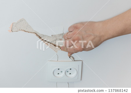 Damaged Wall Plaster Being Removed Near Electrical Socket Showing Cracks and Repair Needs in White Interior Setting Damaged Wall Plaster Being Removed Near Electrical Socket Showing Cracks and Repair Needs in White Interior Setting 137868142