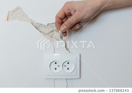 Hand Peeling Cracked Wall Paint Above White Electrical Socket Showing Drywall Damage Repair Concept Hand Peeling Cracked Wall Paint Above White Electrical Socket Showing Drywall Damage Repair Concept 137868143