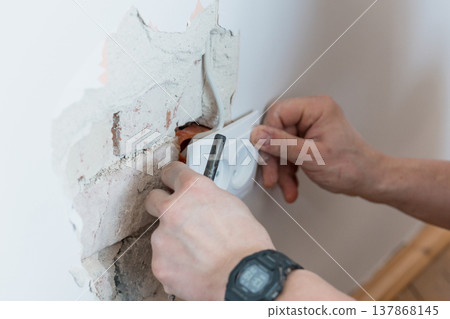 Electrician Installing Wall Socket in Damaged Concrete with Exposed Wires and Tools Showing White Outlet Against Rough Gray Texture Electrician Installing Wall Socket in Damaged Concrete with Exposed Wires and Tools Showing White Outlet Against Rough Gray Texture 137868145