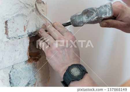 Construction Worker Using Hammer and Chisel on White Brick Wall to Expose Wiring While Wearing Digital Watch During Renovation Project Construction Worker Using Hammer and Chisel on White Brick Wall to Expose Wiring While Wearing Digital Watch During Renovation Project 137868149
