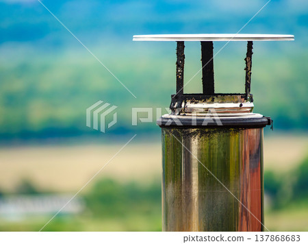 Chimney cap on a metal pipe in a rural area during daylight hours with blurred green background 137868683