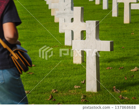 Graves with white crosses in rows on green grass in a memorial cemetery. Person visiting a grave. Graves with white crosses in rows on green grass in a memorial cemetery. Person visiting a grave. 137868688