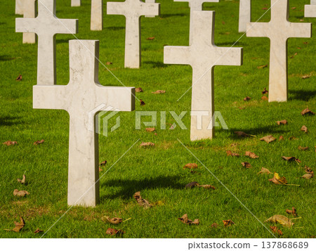 Graves with white crosses arranged in rows on green grass in a memorial cemetery during daylight hours Graves with white crosses arranged in rows on green grass in a memorial cemetery during daylight hours 137868689