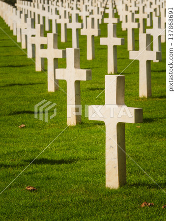 Graves with white crosses arranged in rows on green grass in a memorial cemetery during daylight hours Graves with white crosses arranged in rows on green grass in a memorial cemetery during daylight hours 137868691