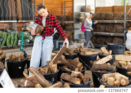 Young woman choosing firewood in store Young woman choosing firewood in store 137868747