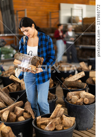 Young woman buys bundle of firewood at hardware store Young woman buys bundle of firewood at hardware store 137868772