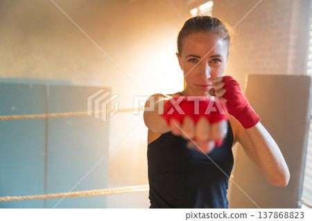 Women self defense girl power. Strong woman fighter punching with red boxing wraps sports protective bandages. Girl punching training punches looking concentrated straight. Fit body workout 137868823