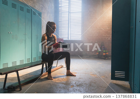 Women self defense girl power. Woman fighter preparing for fight puts on boxing gloves in locker room. Strong girl training punches ready for fight active exercise sparring workout training in gym Women self defense girl power. Woman fighter preparing for fight puts on boxing gloves in locker room. Strong girl training punches ready for fight active exercise sparring workout training in gym 137868831