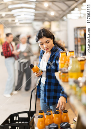 Girl chooses orange juice while standing near shelves hypermarket Girl chooses orange juice while standing near shelves hypermarket 137868863