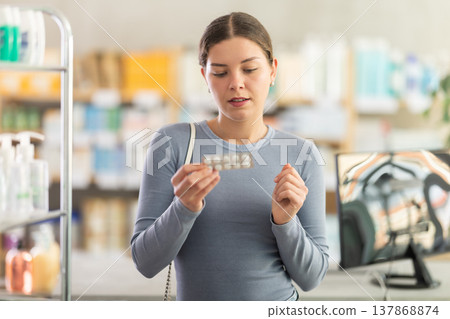 Young woman examining blister pack of paracetamol tablets at pharmacy Young woman examining blister pack of paracetamol tablets at pharmacy 137868874