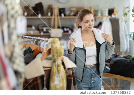 Woman trying on a down jacket with a fur collar in a store Woman trying on a down jacket with a fur collar in a store 137868882