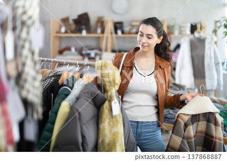 Young woman chooses plaid jacket in clothing store Young woman chooses plaid jacket in clothing store 137868887