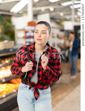 Visiting store woman is looking at something on shelf of showcase, client buy goods 137868907