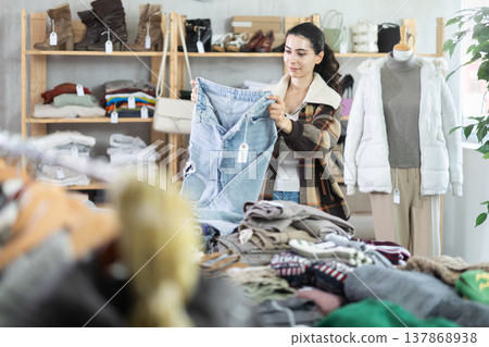 Armenian woman near showcase examine goods, buying jeans trousers Armenian woman near showcase examine goods, buying jeans trousers 137868938