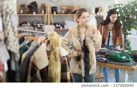Girl try on fur coat in store and carefully examines her reflection in mirror 137868940