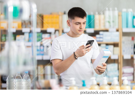 Attentive young guy buyer scanning qr code for box of ointment or gel in pharmacy Attentive young guy buyer scanning qr code for box of ointment or gel in pharmacy 137869104