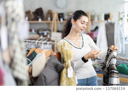 Female shopper chooses and try beautiful checkered coat-jacket in clothing store Female shopper chooses and try beautiful checkered coat-jacket in clothing store 137869159