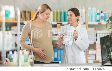 Pharmacist helping pregnant woman to choose baby diapers in pharmacy 137869200