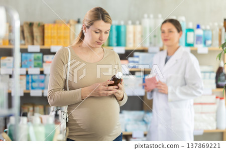 Pregnant woman choose cough syrup in pharmacy, pharmacist recommend similar item in background Pregnant woman choose cough syrup in pharmacy, pharmacist recommend similar item in background 137869221