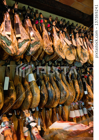 Row of dangling legs jamon with labels on showcase of butcher shop Row of dangling legs jamon with labels on showcase of butcher shop 137869241