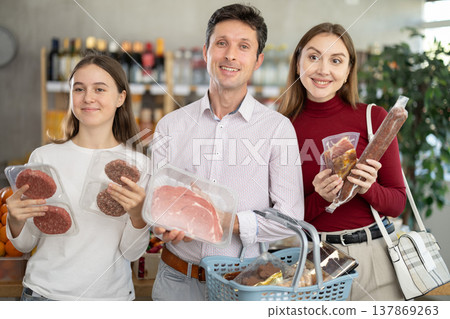 Dad, mom and daughter choose raw meat product and dry sausage in shop 137869263