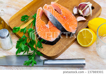 Raw salmon steaks on wooden cutting board with greens, lemon and garlic 137869301