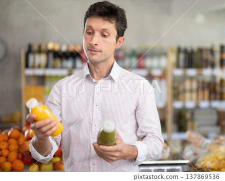Adult man chooses yellow and green smoothie Adult man chooses yellow and green smoothie 137869536