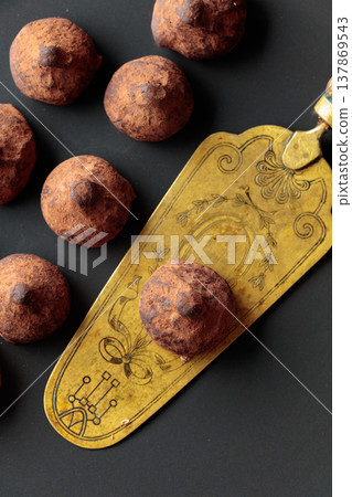 Chocolate truffles and vintage brass cake server on a black plate. Chocolate truffles and vintage brass cake server on a black plate. 137869543