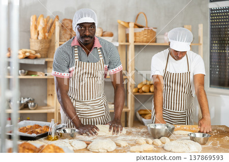 Chef man rolls out dough with rolling pin, male cook creates bun from dough, shapes baking product Chef man rolls out dough with rolling pin, male cook creates bun from dough, shapes baking product 137869593