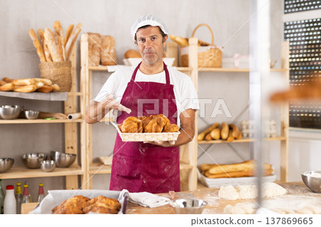 Caucasian male cook-baker worker with basket of croissant, shows many products 137869665