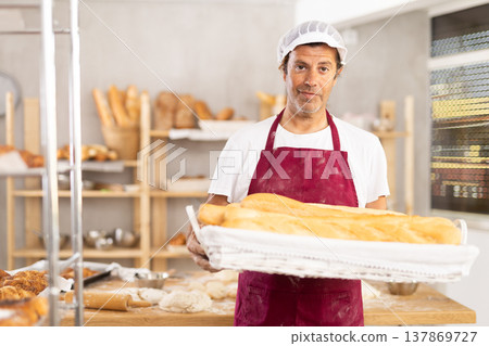 Caucasian male cook-baker worker with basket of baguettes, shows many products 137869727