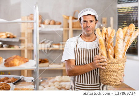 Caucasian male cook-baker worker with basket of baguettes, shows many products Caucasian male cook-baker worker with basket of baguettes, shows many products 137869734