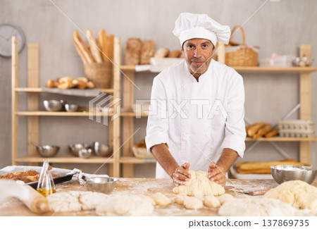 Adult male baker kneading dough on table 137869735