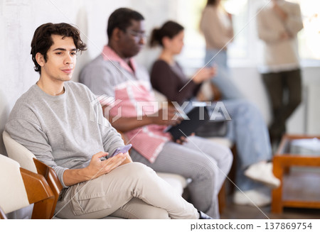 Focused young guy in the lobby of a large company, waiting for her turn to go to office Focused young guy in the lobby of a large company, waiting for her turn to go to office 137869754