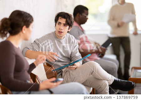 Young guy and woman talking while sitting in waiting area Young guy and woman talking while sitting in waiting area 137869759