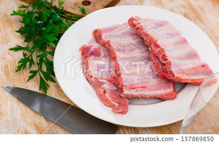 Unprepared pork ribs chopped and ready-to-cook served on white plate decorated with parsley Unprepared pork ribs chopped and ready-to-cook served on white plate decorated with parsley 137869850