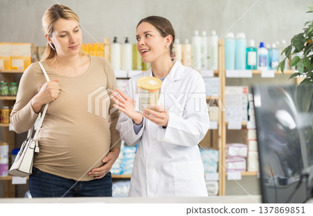 In drug store, pregnant woman examines formula for feeding, pharmacist consulting client In drug store, pregnant woman examines formula for feeding, pharmacist consulting client 137869851