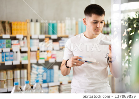 Attentive young guy buyer choosing medical ointment and reading composition of medicine on box in pharmacy Attentive young guy buyer choosing medical ointment and reading composition of medicine on box in pharmacy 137869859