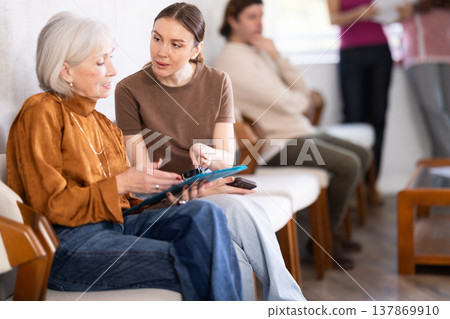 Mature woman talking to young woman while sitting in waiting area Mature woman talking to young woman while sitting in waiting area 137869910