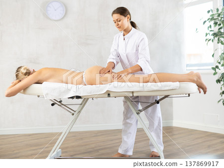 Female masseur performs stroking during spa procedure of thigh buttocks area for girl Female masseur performs stroking during spa procedure of thigh buttocks area for girl 137869917