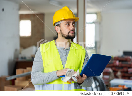An architect in protective hard hat and yellow vest checks room renovation plan using laptop 137869929