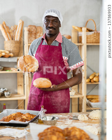 Male baker with basket of baked goods behind bakery counter inviting to buy bread Male baker with basket of baked goods behind bakery counter inviting to buy bread 137869933