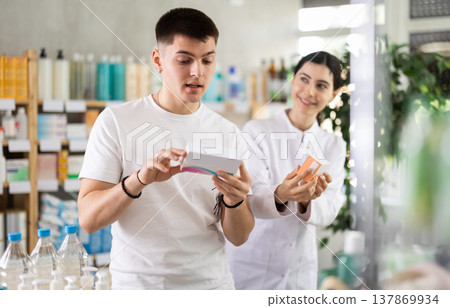 Young man buys pills at drug store, pharmacist in background Young man buys pills at drug store, pharmacist in background 137869934