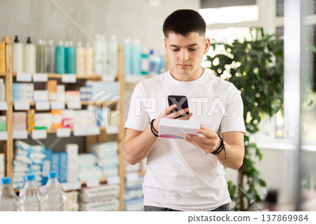 Young man in pharmacy scans QR code on tablets box Young man in pharmacy scans QR code on tablets box 137869984