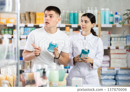 Man chooses mouthwash in modern pharmacy. Female pharmacist helps with choosing Man chooses mouthwash in modern pharmacy. Female pharmacist helps with choosing 137870006