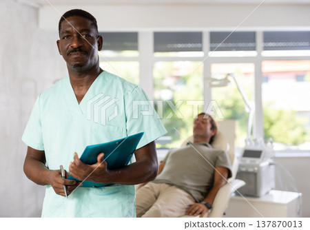 African American cosmetologist standing with clipboard in aesthetic medicine clinic 137870013