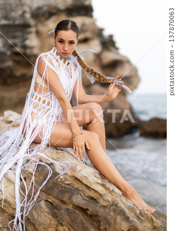 Girl on seashore in sexy and revealing carnival costume sitting on stone 137870063