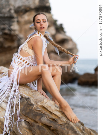 Girl on seashore in sexy and revealing carnival costume sitting on stone Girl on seashore in sexy and revealing carnival costume sitting on stone 137870094