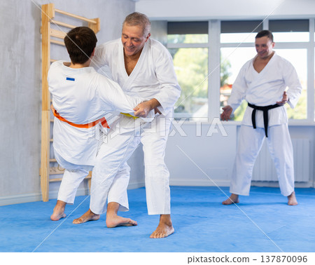 Men of different ages train to make throws on the mat under the guidance of judo coach Men of different ages train to make throws on the mat under the guidance of judo coach 137870096