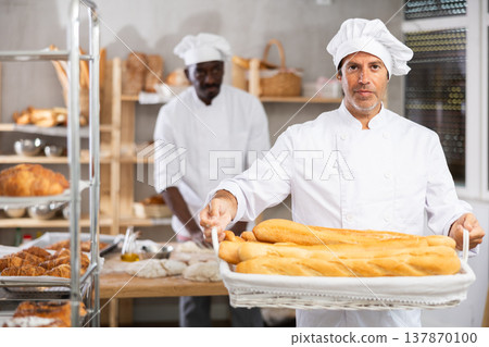 Caucasian male cook-baker worker with basket of baguettes, shows many products 137870100